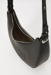 Sac à épaule en cuir noir avec une texture lisse, une forme incurvée, une fermeture éclair en métal argenté et des détails en relief à l'avant. L'intérieur est beige.