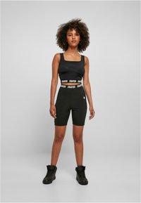 Crop top de sport noir avec un décolleté carré et une bande avec logo. Short de vélo noir assorti, tous deux en matériau extensible. Baskets montantes noires.