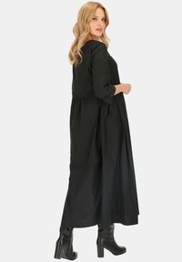 Czarna, długa sukienka maxi z długim rękawem, dopasowaną górą i zwiewnym dołem, wykonana z lekkiego materiału. Posiada miękką fakturę i skromny dekolt.