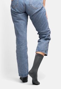Calcetín gris hasta la rodilla hecho de material suave, con un pequeño logo en el puño. Combinado con unos vaqueros de color azul claro remangados.