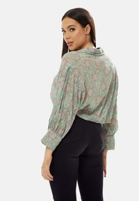 Green floral blouse with a relaxed fit, featuring puffed sleeves, a collar, and a lightweight fabric. Paired with fitted black pants.