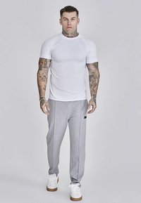 Bela oprijeta majica s kratkimi raglan rokavi, kombinirana s svetlo sivimi trenirkami z majhno črno etiketo in belimi supergami.