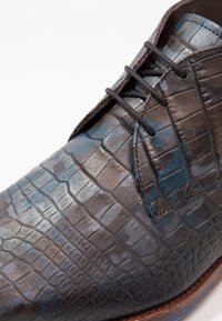 Chaussure à lacets pour hommes en cuir texturé gris foncé avec un motif de peau de crocodile ; présente des accents bleus et une semelle marron.