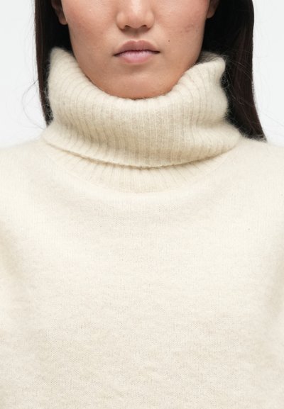 Κρέμας χρώματος πουλόβερ με ψηλό γιακά, φτιαγμένο από απαλό, ριγωτό πλεκτό υλικό. Διαθέτει ψηλό αναδιπλωμένο γιακά και χαλαρή εφαρμογή.