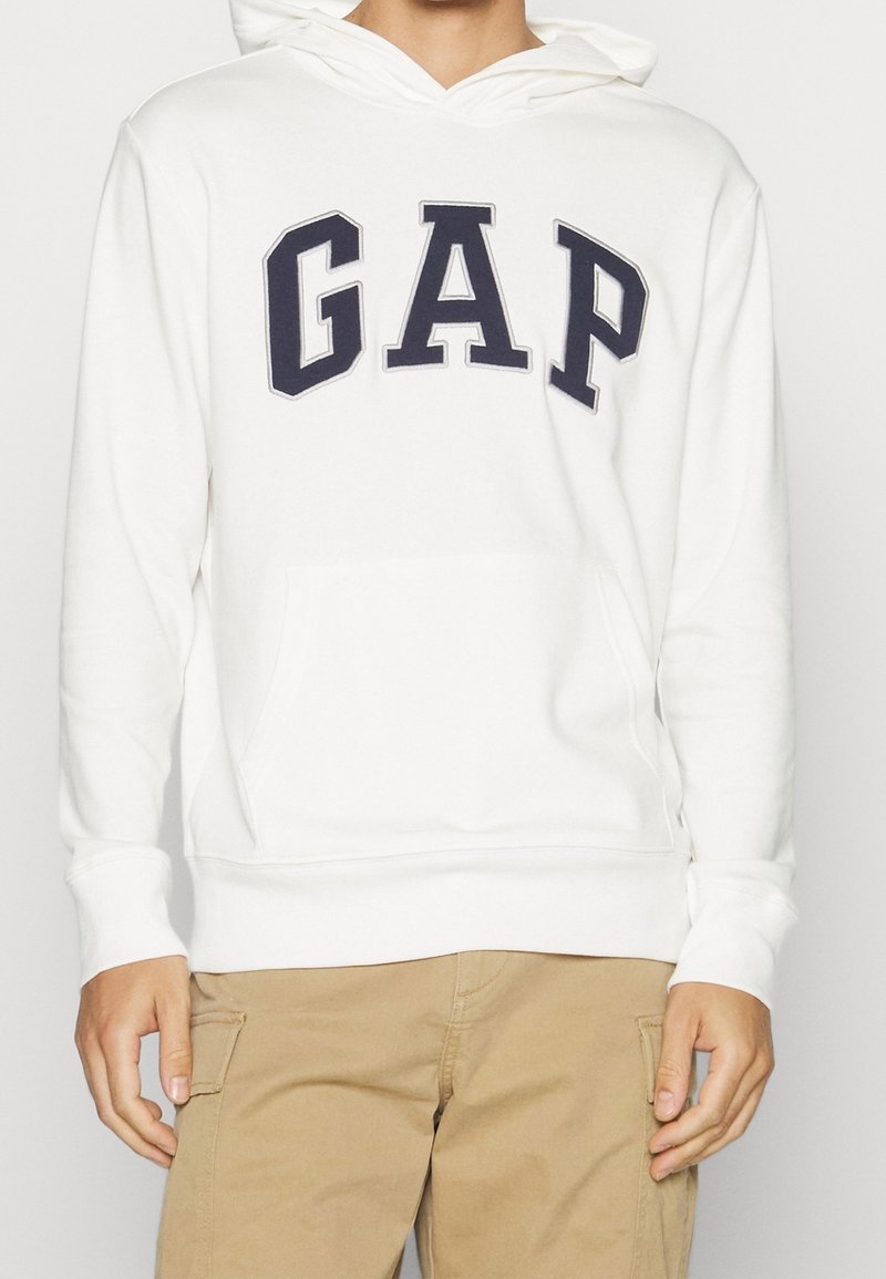 Felpa bianca in misto cotone, presenta un grande logo "GAP" blu navy, tasca a marsupio frontale e cappuccio con cordino, con polsini a coste.