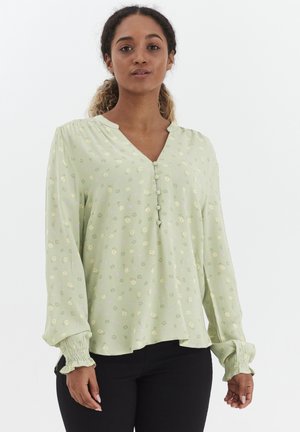 Hellgrüne Bluse mit V-Ausschnitt, langen Ärmeln und gerafften Manschetten. Verfügt über kleine Blumenmuster in Gelb und Lila. Knopfdetails vorne.