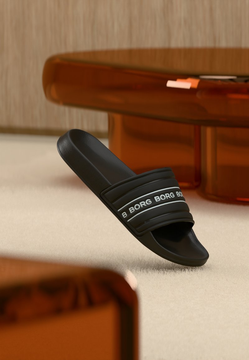 Μαύρο σανδάλι slide με την επιγραφή "BORG" στο λουρί, τοποθετημένο πάνω σε μπεζ χαλί κοντά σε διαφανή πορτοκαλί πόδια επίπλων.