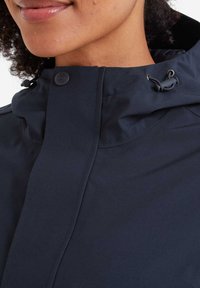 Navy waterproof jacket featuring a high collar, snap closure, adjustable drawcord, and smooth texture with stitching details.