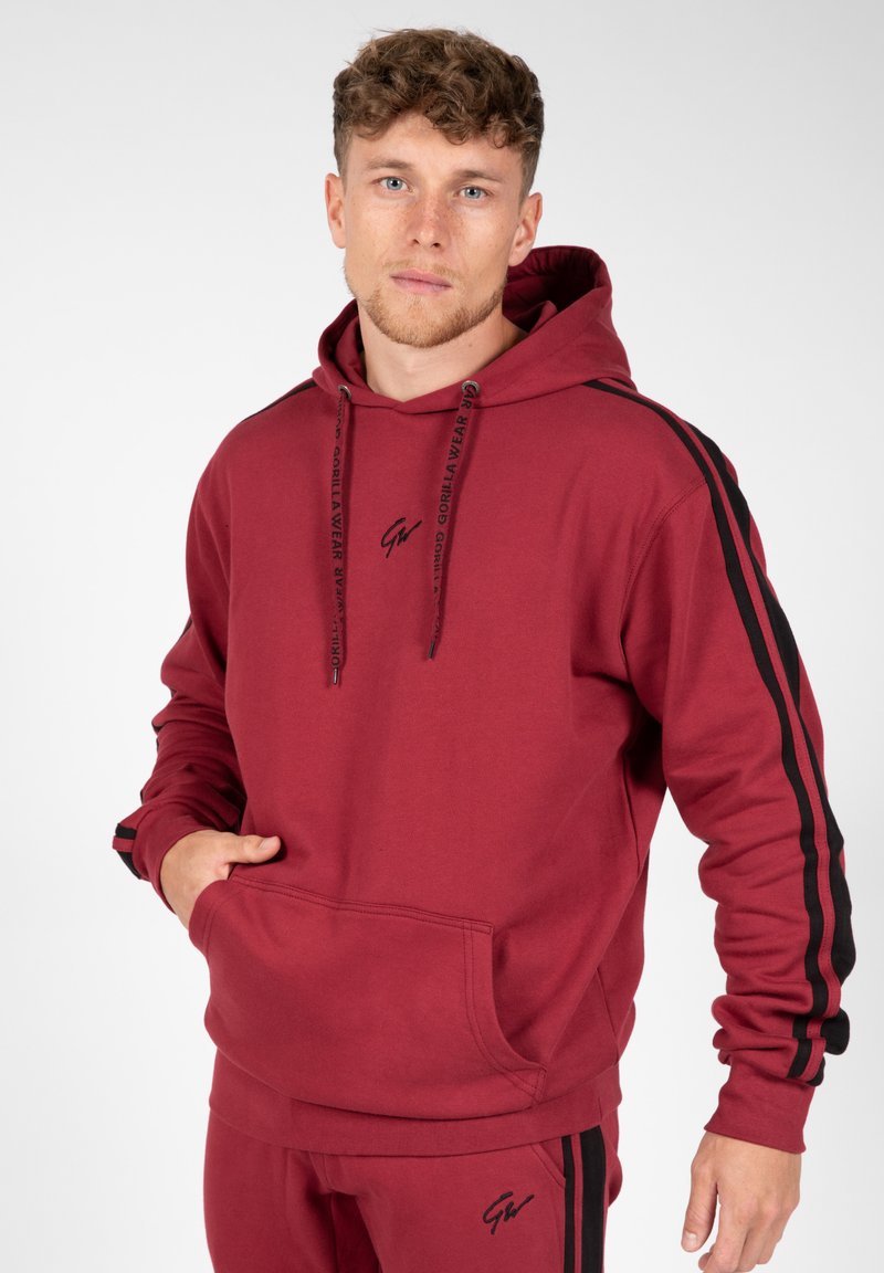 Bordeauxkleurige hoodie met een kangoeroezak, trekkoordcapuchon, zwarte zijstrepen en logo aan de voorkant. Gemaakt van een gestructureerde stof.