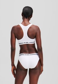 Ensemble de soutien-gorge de sport et de culotte en coton blanc avec une bande de logo noir, doté d'un design dos nageur. Texture lisse, forme ajustée, style minimaliste.
