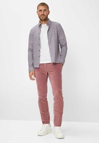 Camicia a quadri blu e rossa, con una t-shirt bianca sotto, abbinata a pantaloni in velluto a coste rosa e sneakers bianche. La camicia ha bottoni e maniche lunghe.