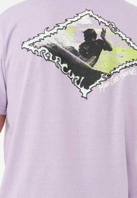 Camiseta corta de manga corta de color púrpura claro con un estampado gráfico de un surfista y olas estilizadas, bordeadas por un diseño de marco dentado.