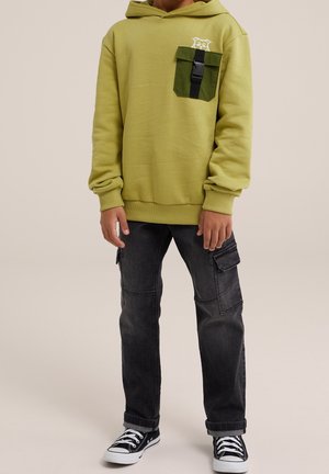 Sweat à capuche vert avec une poche avant et une attache noire, associé à un pantalon cargo gris foncé et des baskets noires et blanches. Texture lisse.