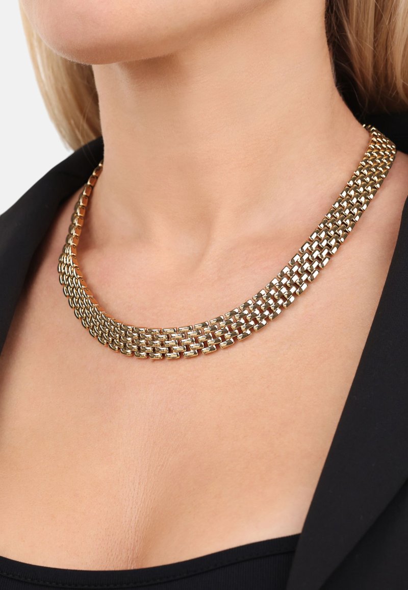 Guldkedja med flätad design, bestående av flera rader och en slät textur. Buren mot en svart topp, vilket framhäver dess metalliska lyster.