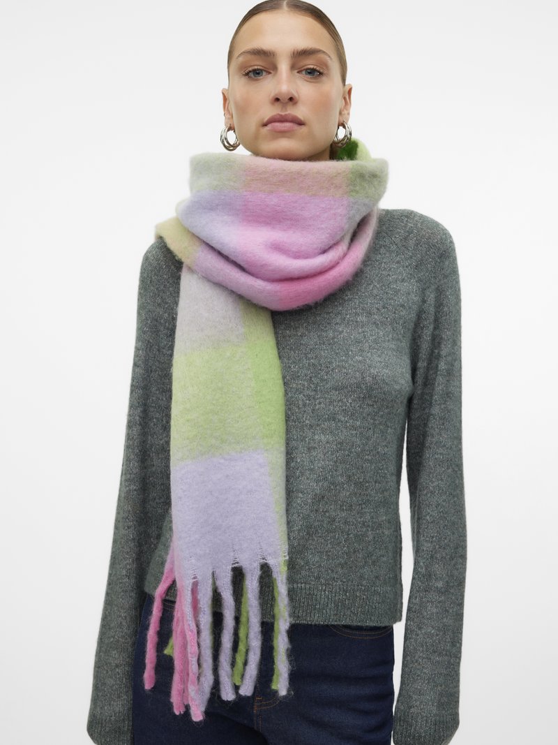 Nő ezüst karika fülbevalóval, zöld kötött pulóverben és bolyhos, pasztell színű sállal, amely rózsaszín, zöld és lila blokkokból áll, a nyaka köré van tekerve.