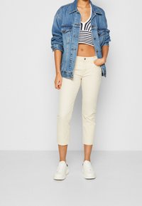 Blauwe spijkerjack, zwart-wit gestreept cropped gebreid topje, crèmekleurige cropped broek en witte sneakers.