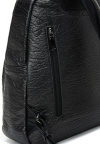 Zwarte leren tas met een gestructureerde afwerking, zijrits vak en een afneembare schouderband. Het ontwerp is gestroomlijnd met een ronde vorm.