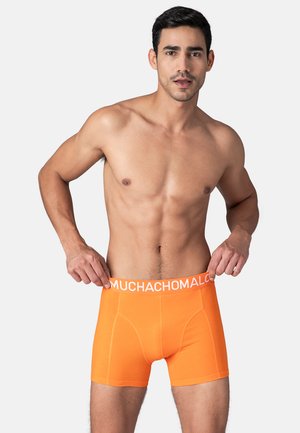 Narančaste bokserice od mekog materijala s bijelim elastičnim pojasom koji nosi naziv branda "MUCHACHOMALO."