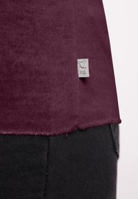 Bordeaux gebreid t-shirt met een gestructureerde stof, een rafelige zoom en een klein grijs stoffen label met een hondenafbeelding.