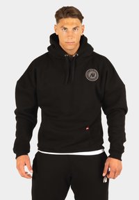 Zwarte hooded sweatshirt met een grote capuchon, voorzak en een cirkelvormig logo op de borst. Gemaakt van een gestructureerde katoenen stof.