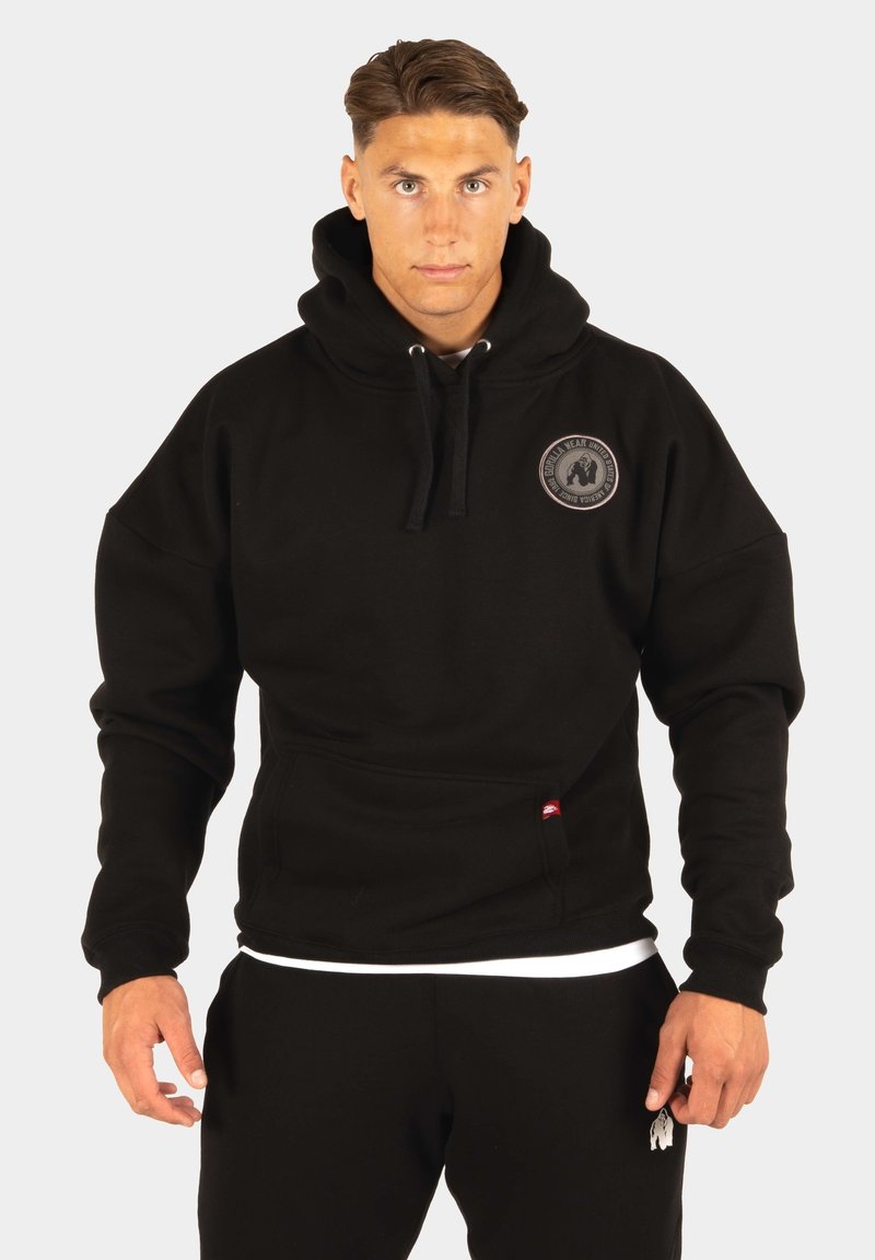Zwarte hooded sweatshirt met een grote capuchon, voorzak en een cirkelvormig logo op de borst. Gemaakt van een gestructureerde katoenen stof.