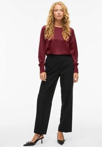 Blusa lunga in raso bordeaux con maniche a sbuffo, abbinata a pantaloni neri a gamba larga e scarpe nere con tacco. Design minimalista, colori solidi.