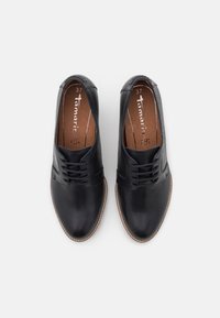 Zapatos de cuero negro con un acabado suave, corte bajo, diseño con cordones y detalle de costura marrón claro alrededor de la suela de goma. Talla 37.