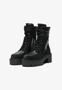 Schwarze Kampfstiefel aus einer Mischung von Leder und Wildleder, mit Schnürdesign, dicker Plateausohle und Lammfellakzenten am Kragen.
