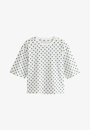 Hvid T-shirt med korte ærmer, sorte polkaprikker, rund hals og en løs, kasseformet pasform.