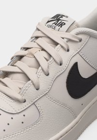 Κοντινή λήψη λευκού αθλητικού παπουτσιού Nike Air Force 1 που δείχνει το υφασμάτινο δέρμα, τα κορδόνια και το μαύρο λογότυπο Nike swoosh.
