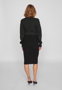 Zwarte trui met verzamelde mouwen, gecombineerd met een zwarte geribbelde midi-rok. De outfit heeft een getailleerde pasvorm en een enkellange ontwerp.