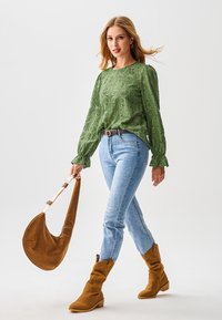 Groen kanten blouse met lange mouwen, blauwe aansluitende spijkerbroek, bruine enkellaarsjes en een bruine slordige schoudertas met een witte riem.