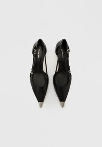 Zapatos de piel negra con punta afilada y diseño de tiras traseras, con puntera metálica plateada y correa ajustable con detalle de hebilla.