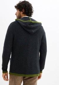 Cardigan con cappuccio in tessuto navy strutturato con accenti verdi sul cappuccio e sui polsini. Offre una vestibilità rilassata con tasche laterali e orli a costine.