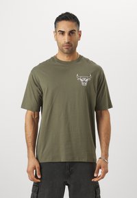 Oliven grøn bomulds-t-shirt med korte ærmer, der har et hvidt oksegraphic på brystet. Enkel design og afslappet pasform.