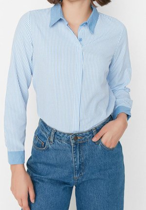 Lichtblauw-wit gestreept overhemd met knopen, met een contrasterende effen lichtblauwe kraag en manchetten, gecombineerd met een high-waisted blauwe spijkerbroek.