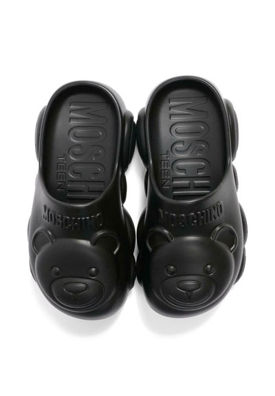 Sabots à enfiler Moschino Teen noirs avec des visages d'ours en peluche embossés et le nom de la marque sur le dessus, semelle rembourrée visible à l'intérieur.