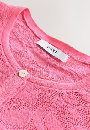 Cardigan roz tricotat cu un model texturat de dantelă, având un decolteu rotund și o singură închidere cu nasture. Eticheta poartă inscripția "NEXT".