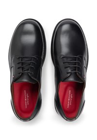 Μαύρα δερμάτινα παπούτσια με λεία υφή, σχέδιο με κορδόνια και κόκκινη επένδυση με λογότυπο. Στρογγυλεμένη μύτη και ελάχιστα μεταλλικά διακοσμητικά στοιχεία.