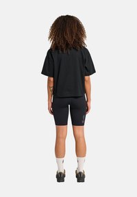 Svart bomullströja med avslappnad passform, kombinerad med svarta cykelshorts. Synlig tatuering på armen och mönstrade strumpor. Enkla skor.