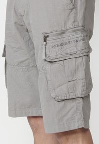 Shorts cargo gris clair en tissu texturé. Comprend plusieurs poches, y compris une poche latérale zippée, et des coutures renforcées.