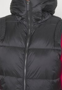 Czarna pikowana kamizelka z wysokim kołnierzem i zamkiem błyskawicznym, cechująca się pikowaną fakturą oraz przeszyciami na ramionach, lekka i odporna na warunki pogodowe.