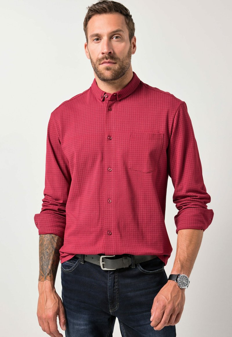 Rode overhemdd blouse met een subtiele geometrische print, lange mouwen opgerold, en een borstzak. Draag het met donkere jeans en een horloge.