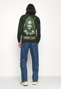 Black long-sleeve shirt featuring a graphic of a masked figure with green accents, paired with blue cargo pants and colorful sneakers.
