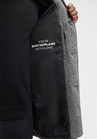 Blazer a motivo houndstooth grigio con rivestimento in satin nero, caratterizzato da testo bianco che recita "DA SVIZZERA CON AMORE." Vestibilità su misura, design strutturato.