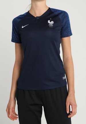 Maglia sportiva blu navy con maniche testurizzate blu scuro, logo Nike sul lato destro del petto e emblema di un gallo bianco sul lato sinistro del petto.