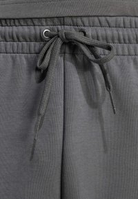 Šedé tepláky s elastickým pásom na šnúrku, textúrovanou tkaninou a voľným strihom. Obsahujú oká na šnúrku a celkovú hladkú povrchovú úpravu.