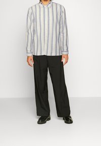 Camisa de rayas de manga larga en azul claro y blanco, con botones y cuello, combinada con pantalones negros holgados y zapatos negros.