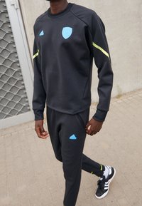 Felpa sportiva nera e pantaloni con loghi e dettagli azzurri. La felpa ha maniche lunghe, polsini a costine e colletto tondo.