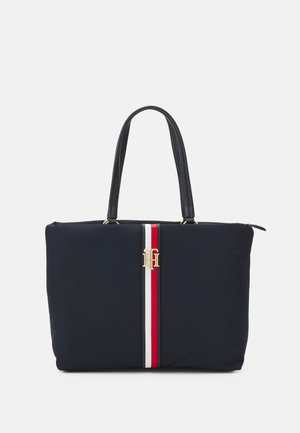 Marineblaues Nylon-Tragetasche mit schwarzen Ledergriffen, die einen zentralen rot-weißen Streifen und ein goldfarbenes Logo-Highlight auf der Vorderseite aufweist.